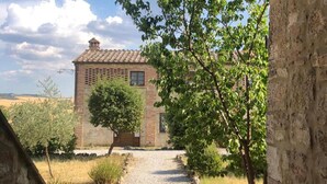 A rustic stone building with a tiled roof, a gravel path leading to it, and surrounding greenery.