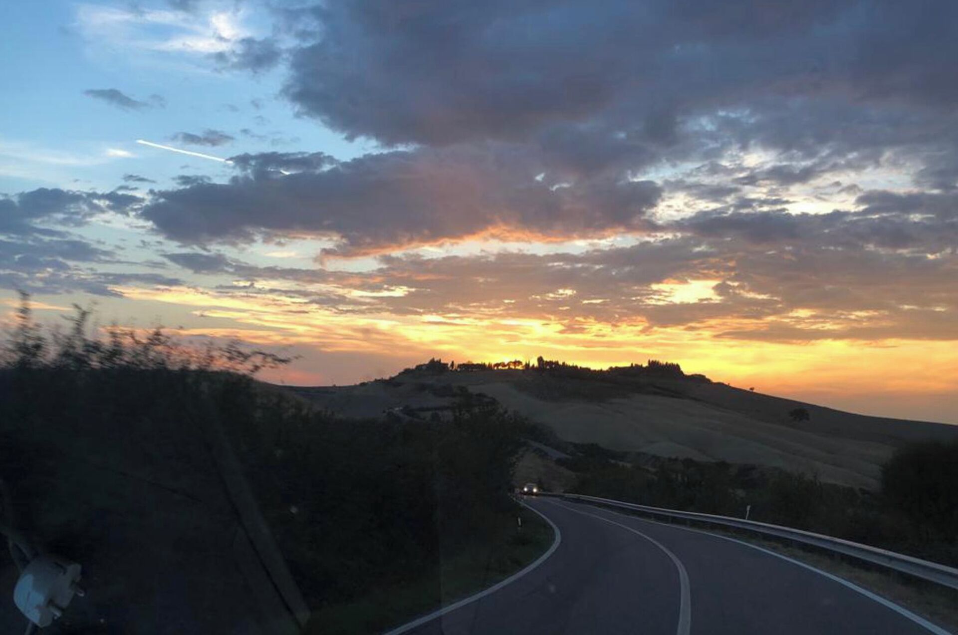 A winding road curving through a hilly landscape with a sunset in the background.