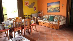 A dining area with wooden chairs and a table set for two, a sofa with floral upholstery, and a painting of sunflowers on the wall.