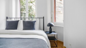 Une chambre à coucher avec un lit, deux fenêtres, une table de chevet et une lampe.