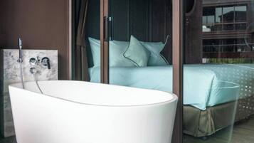 Een moderne badkamer met een vrijstaand bad, een douchecabine met glazen wanden en een bed met een lichtblauwe sprei.