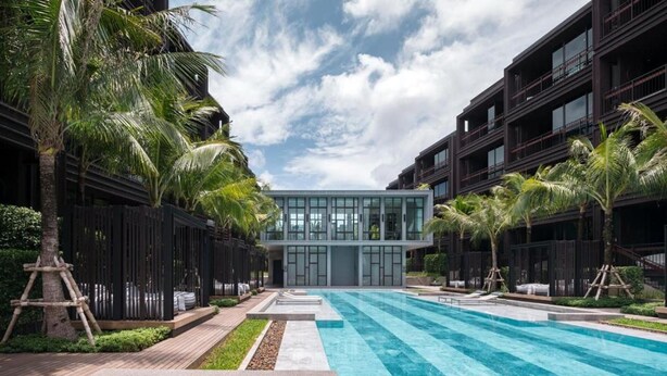 Un edificio moderno con piscina en primer plano, rodeado de palmeras y un cielo despejado.