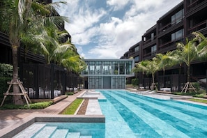 A modern building with a pool in the foreground, surrounded by palm trees and a clear sky. - Tropical Oasis Retreat in Rawai, Phuket (Rawai)