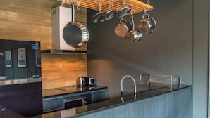 Una cocina moderna con encimera negra, electrodomésticos de acero inoxidable y utensilios colgando.