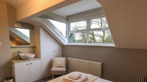 A bedroom with a skylight, a white sink, a chair, and a bed with towels. - Beckmead (Windermere)