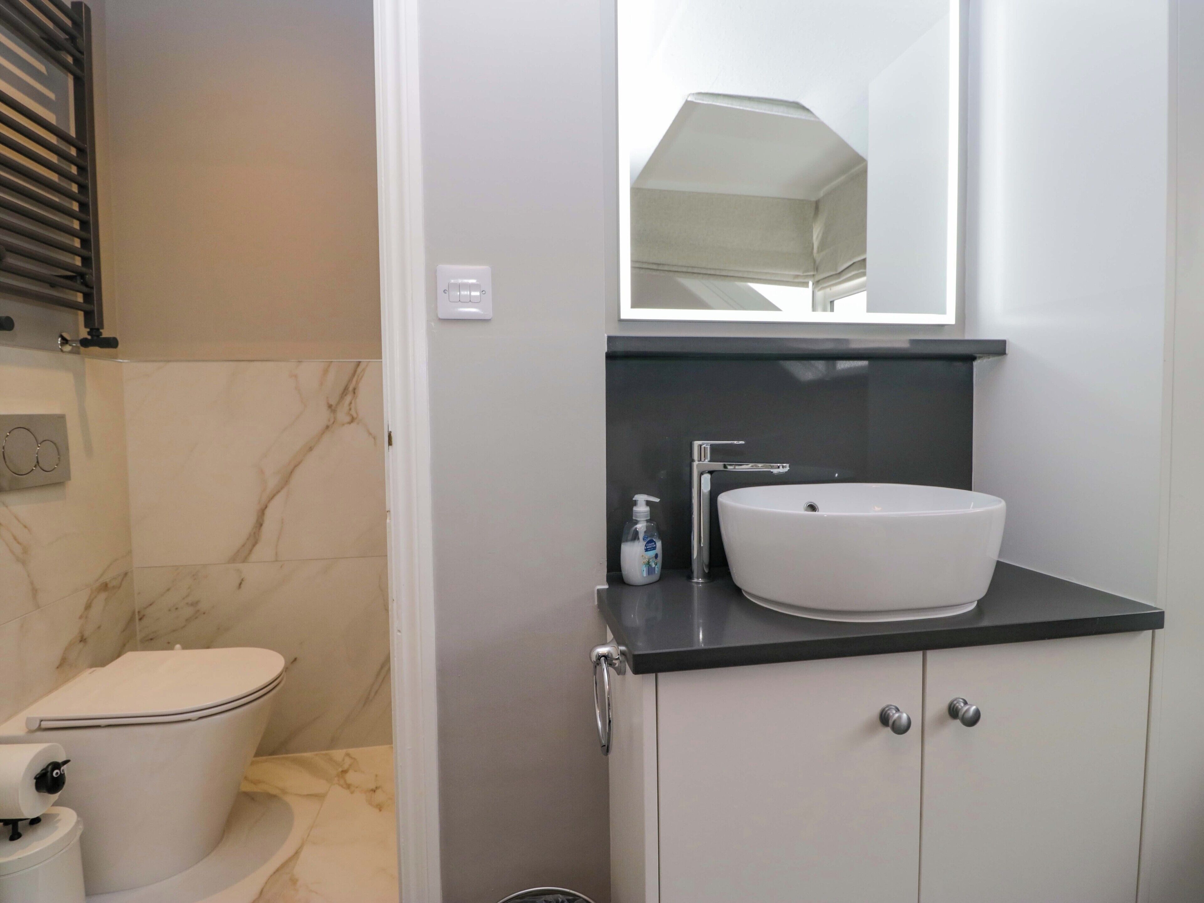 Un bany amb un vàter blanc, un lavabo blanc i un mirall damunt del lavabo.