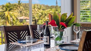 A dining table set with a bottle of wine, glasses, and a vase with red flowers. - STEPS FROM STUNNING MOLOAA BAY (Anahola)