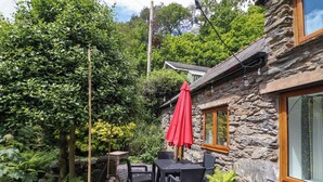 Un edificio de piedra con un marco de ventana de madera, una sombrilla roja y una parrilla de barbacoa en el exterior.