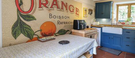Una cocina con una mesa, una cafetera y un mural en la pared que dice "ORANGE".