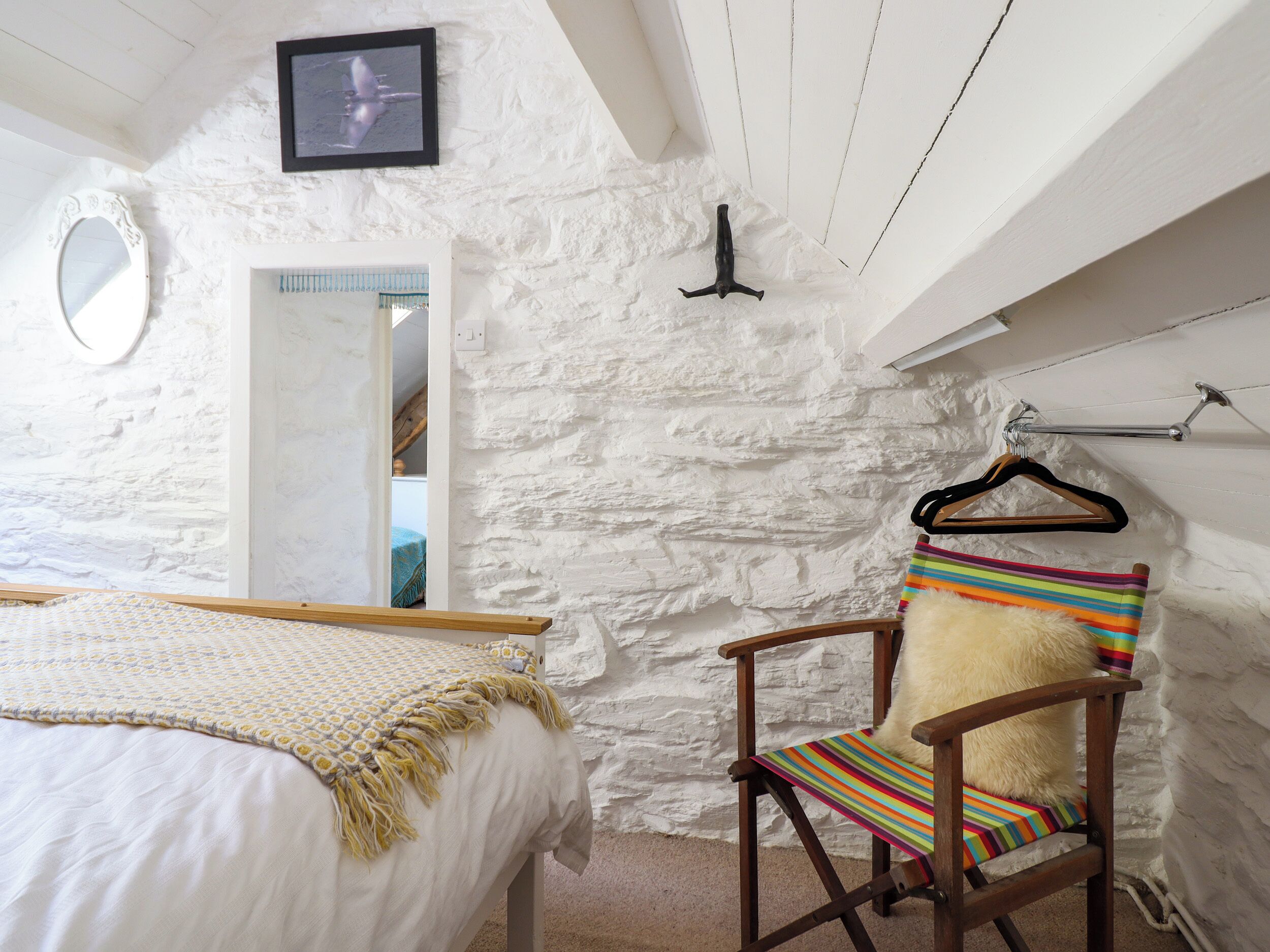 A bedroom with a bed, a chair with a striped cushion, a mirror, and a picture on the wall.