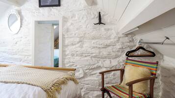 A bedroom with a bed, a chair with a striped cushion, a mirror, and a picture on the wall.