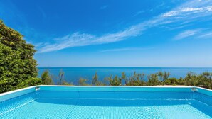 Ein klares, blaues Schwimmbecken mit Blick auf das Meer und Bäume.