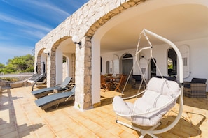A covered outdoor seating area with stone arches, lounge chairs, and a hanging chair. - 2750 Villa Petra by Barbarhouse (Gagliano del Capo)