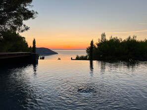 A serene waterfront view with a wooden dock extending into calm waters, surrounded by dense foliage.