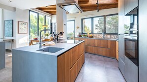 A modern kitchen with a central island, wooden cabinets, and large windows offering views of the outdoors.
