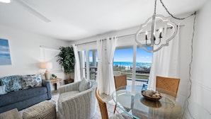 A modern living room with a glass dining table, wicker chairs, and a view of the ocean. - Eastern Shores - 101 1 Bedroom Condo by RedAwning (Santa Rosa Beach)