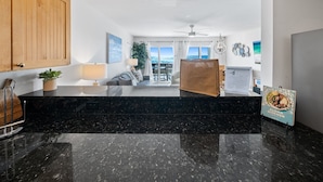 A modern kitchen with black marble countertops, wooden cabinets, and a view to the outside. - Eastern Shores - 101 1 Bedroom Condo by RedAwning (Santa Rosa Beach)