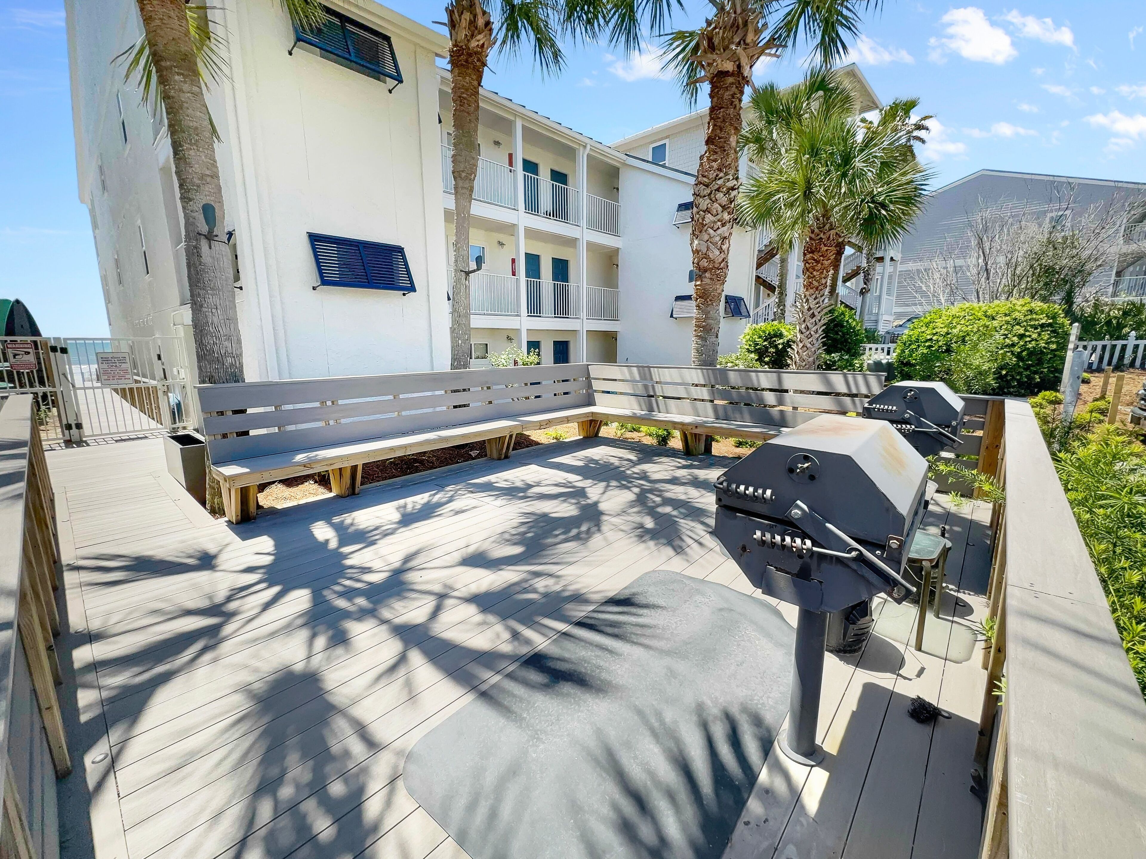 A deck with a barbecue grill, benches, and palm trees.