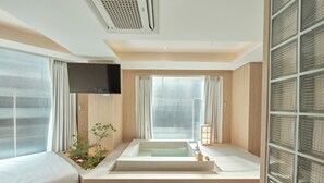 Un baño moderno con una bañera independiente, un televisor de pantalla plana y un amplio ventanal con cortinas.