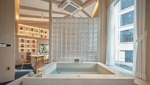Un baño moderno con una bañera grande, estantes de madera con adornos, y un ventanal que proporciona luz natural.