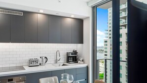 A modern kitchen with grey cabinets, white tiles, and a view of a high-rise building. - Modern High-Rise Condo with Pool/Gym, in Central DT MIAMI! (Miami)