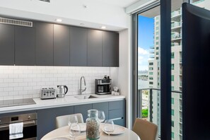 A modern kitchen with grey cabinets, white tiles, and a view of a high-rise building.