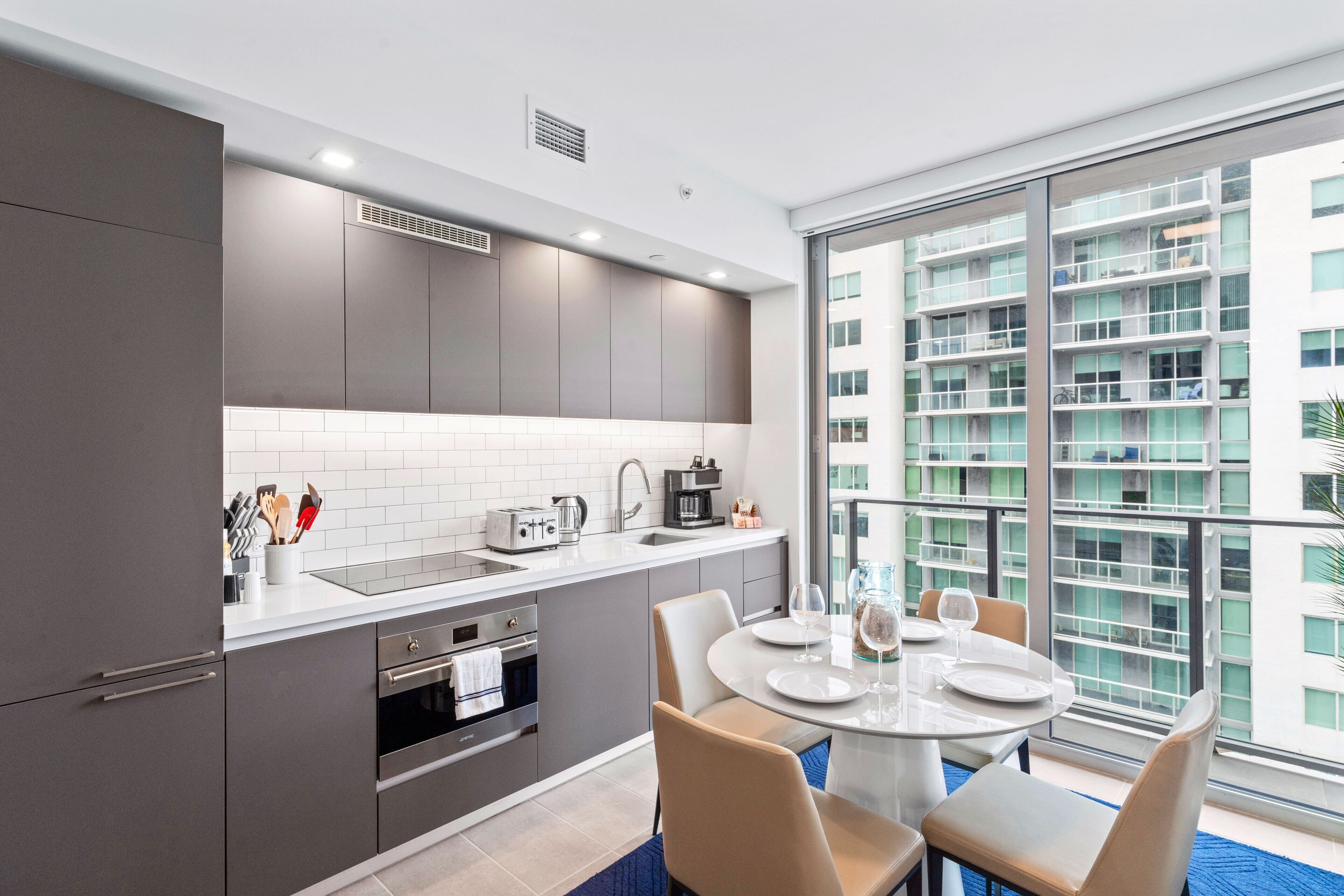 A modern kitchen with grey cabinets, white countertops, and a dining area with a round table and chairs.