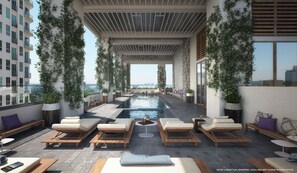 A rooftop pool area with lounge chairs and a central table, surrounded by greenery and overlooking a cityscape. - Modern High-Rise Condo with Pool/Gym, in Central DT MIAMI! (Miami)