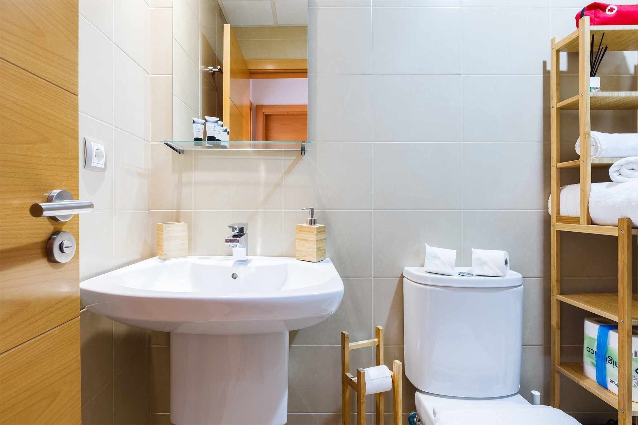Een moderne badkamer met een groot wit wastafel, toilet en een houten plank met handdoeken.