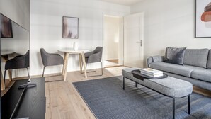 A modern living room with a grey sofa, a round coffee table, and two grey chairs around a small white table. - Mod Wiedikon 2.5 Room w/ Storage & W/D, 1 min to Market, by Blueground (Zurich)