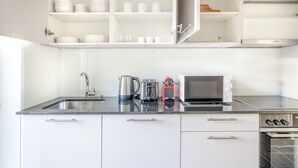A modern kitchen with white cabinets, a stainless steel sink, a kettle, a toaster, and a microwave. - Mod Wiedikon 2.5 Room w/ Storage & W/D, 1 min to Market, by Blueground (Zurich)