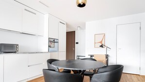 A modern kitchen with white cabinets, a microwave, and a round dining table with four chairs. - Lux Wollishofen 2.5 Room w/ W/D & Storage, 2 min to Market, by Blueground (Zurich)