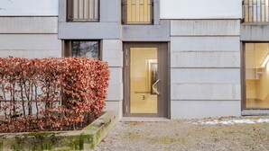 A modern building with a ground-level entrance, a small garden area with autumn foliage, and a door labeled "Spinnereiplatz 3". - Lux Wollishofen 2.5 Room w/ W/D & Storage, 2 min to Market, by Blueground (Zurich)