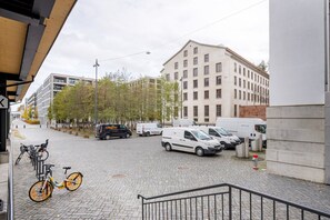 A paved street with parked vehicles, a bicycle, and a building with multiple windows. - Lux Wollishofen 2.5 Room w/ W/D & Storage, 2 min to Market, by Blueground (Zurich)