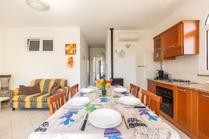 Uma sala de jantar com mesa posta para quatro pessoas, um sofá e uma cozinha com armários de madeira e fogão.