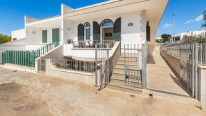 A modern two-story house with a balcony, a gated entrance, and a staircase leading to the upper floor.