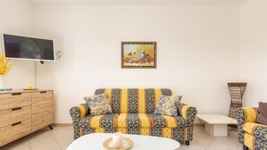A living room with a patterned sofa, a flat-screen TV, a decorative painting, and a small table with a candle.