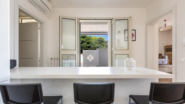 A modern kitchen with a large island, three black chairs, and a view of the outdoors. - 2508 Villetta Blanca by Barbarhouse (Castrignano del Capo)