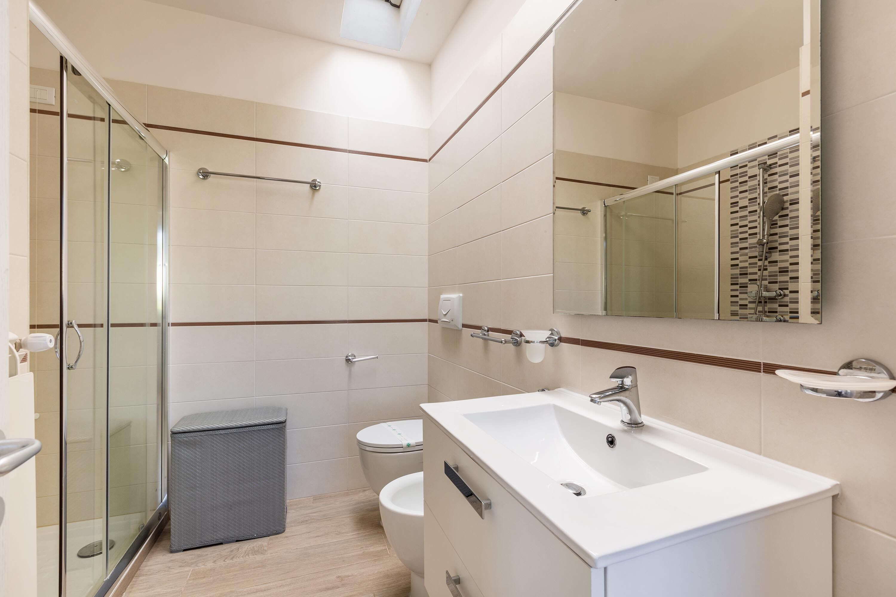 Un baño moderno con cabina de ducha de vidrio, inodoro y lavamanos con espejo.