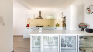 A modern kitchen with white cabinetry, a central island with glass-fronted cabinets, and a decorative clock on the wall. - 2508 Villetta Blanca by Barbarhouse (Castrignano del Capo)