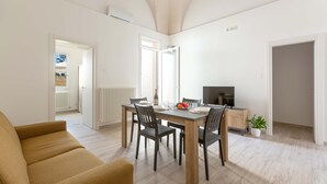 A dining area with a wooden table, four chairs, and a TV on a stand. - 3045 Appartamento Belloluogo by Barbarhouse (Lecce)