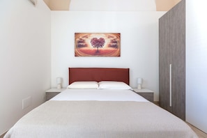 A bedroom with a bed, a red headboard, bedside lamps, and a painting of a tree on the wall.