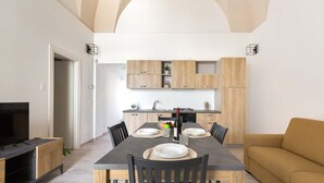 A modern dining area with a rectangular table, six chairs, and a sofa. A television is on a stand to the left. The room has wooden cabinets and a kitchen in the background. - 3045 Appartamento Belloluogo by Barbarhouse (Lecce)