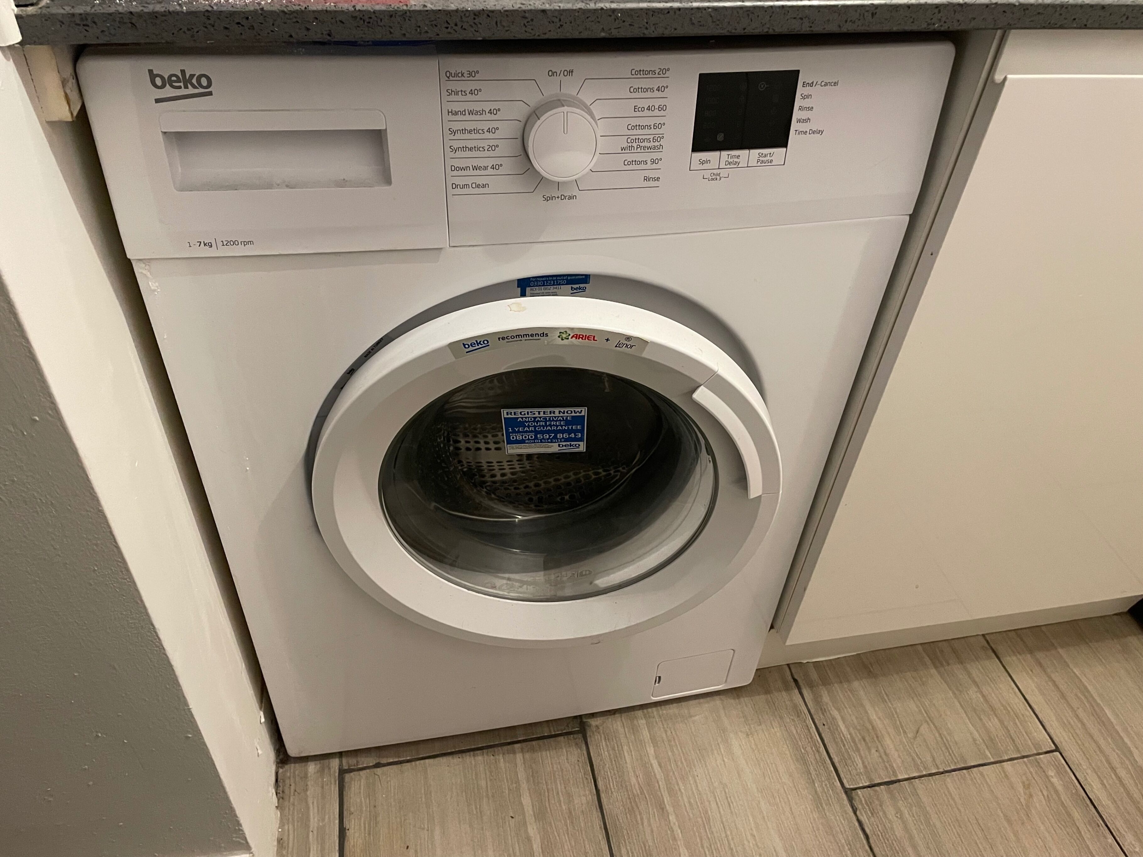 Un lave-linge à chargement frontal doté d’un panneau de commande, d’une étiquette recommandant l’utilisation de la lessive Ariel et d’une étiquette d’enregistrement.