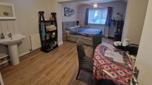 Een slaapkamer met een bed, een bureau, een stoel, een radiator, een plank en een raam met gordijnen.