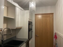 A compact kitchen with a sink, stainless steel appliances, and a wooden door.