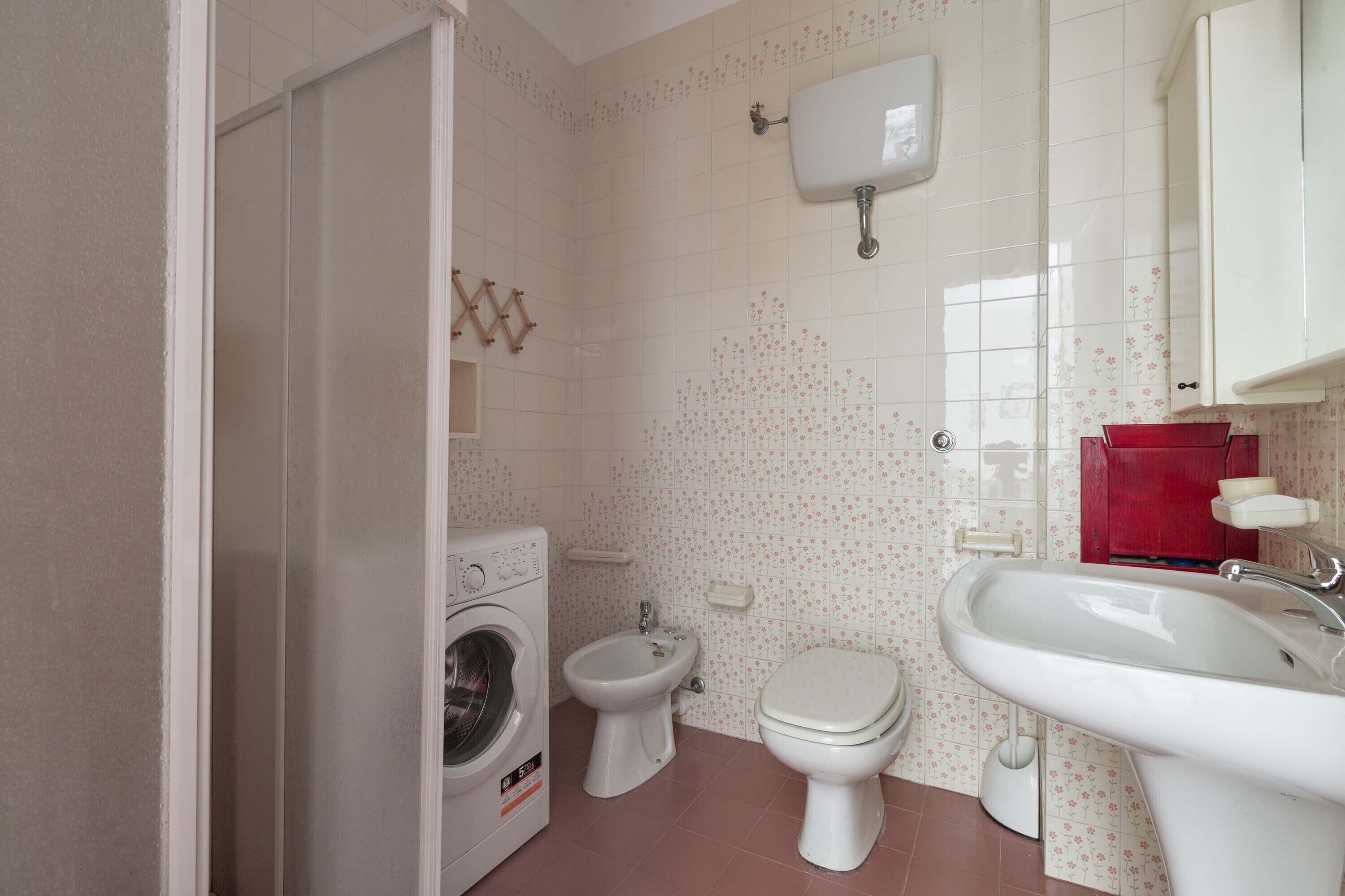 A bathroom with a washing machine, toilet, bidet, and sink.