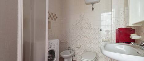 A bathroom with a washing machine, toilet, bidet, and sink.