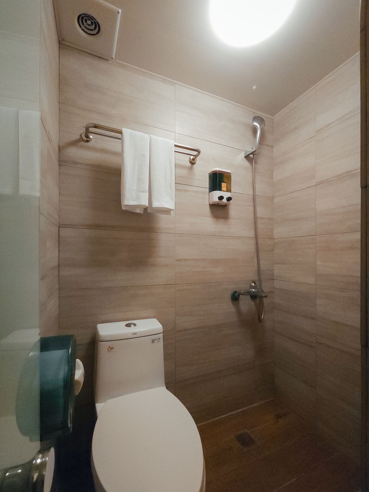 A small, tiled bathroom with a toilet, a towel rack, and a shower.