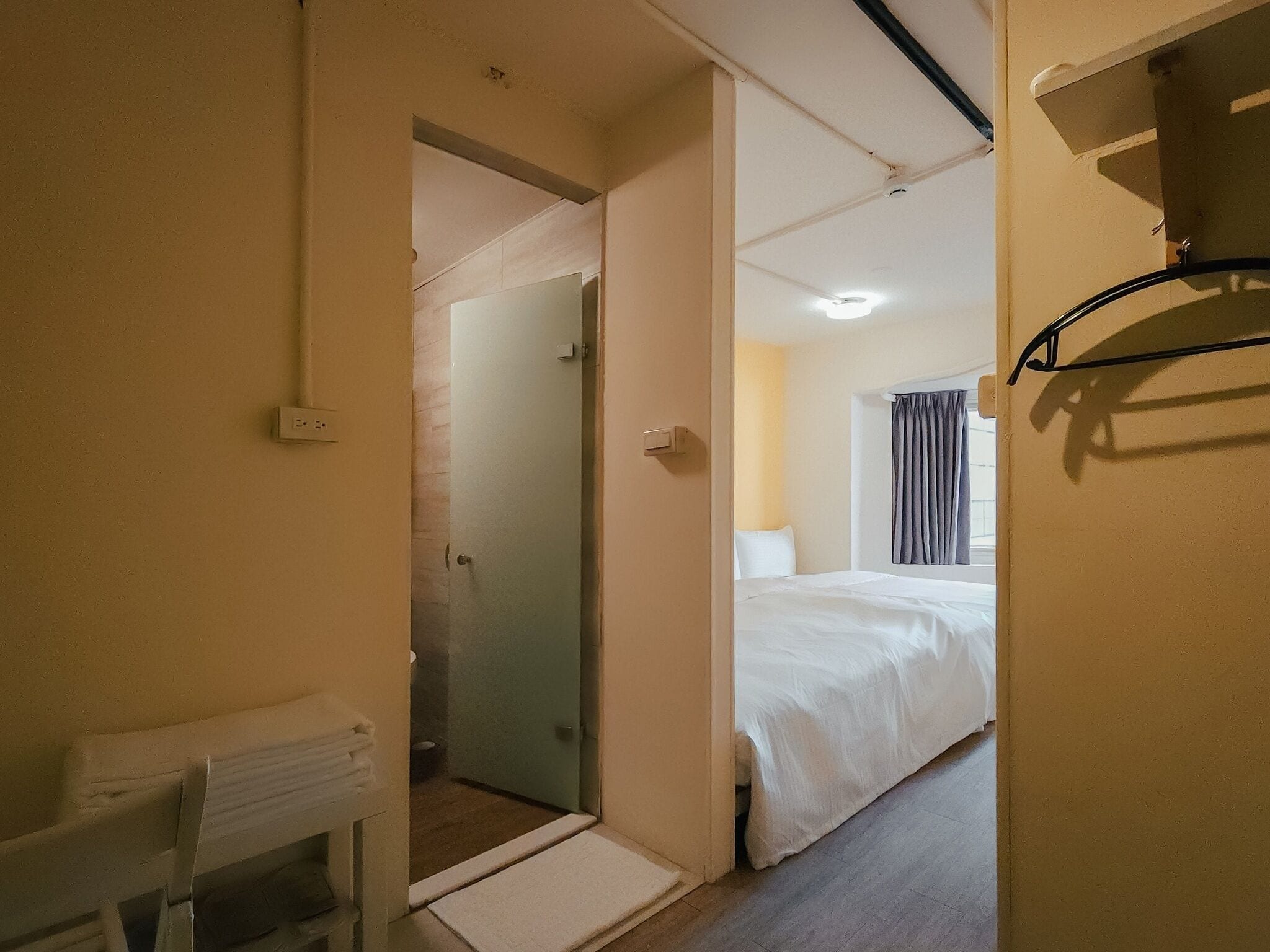 A hotel room with a bed, a small table, and a shower area.